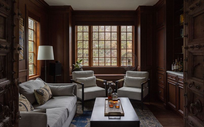 The library, which features original custom wooden doors, maintains a whiskey room vibe thanks to dark oak cabinetry, Bernhardt velvet chairs in soft grey and a Four Hands tufted leather table. An inviting Robin Bruce sofa and elegant Loloi rug round out the sophisticated study The library, which features original custom wooden doors, maintains a whiskey room vibe thanks to dark oak cabinetry, Bernhardt velvet chairs in soft grey and a Four Hands tufted leather table. An inviting Robin Bruce sofa and elegant Loloi rug round out the sophisticated study