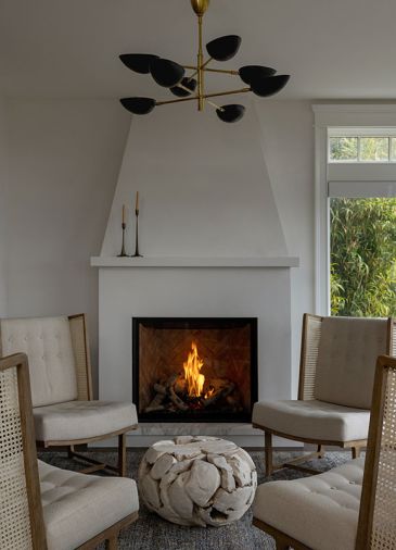 The day room flaunts a cozy fireplace with a custom plaster surround. A distinctive chandelier from Visual Comfort and shifted room orientation allow the homeowners to to fully enjoy the space The day room flaunts a cozy fireplace with a custom plaster surround. A distinctive chandelier from Visual Comfort and shifted room orientation allow the homeowners to to fully enjoy the space