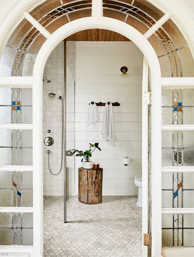 Anne wisely showcased the stunning salvaged stained-glass door discovered at Bloomsbury Art & Fine Antiques for the primary bath’s entry. “Milk Mustache” paint by Dunn Edwards echoes the door’s trim, while Ann Sacks Carrara hex tile grounds the room. Anne wisely showcased the stunning salvaged stained-glass door discovered at Bloomsbury Art & Fine Antiques for the primary bath’s entry. “Milk Mustache” paint by Dunn Edwards echoes the door’s trim, while Ann Sacks Carrara hex tile grounds the room.